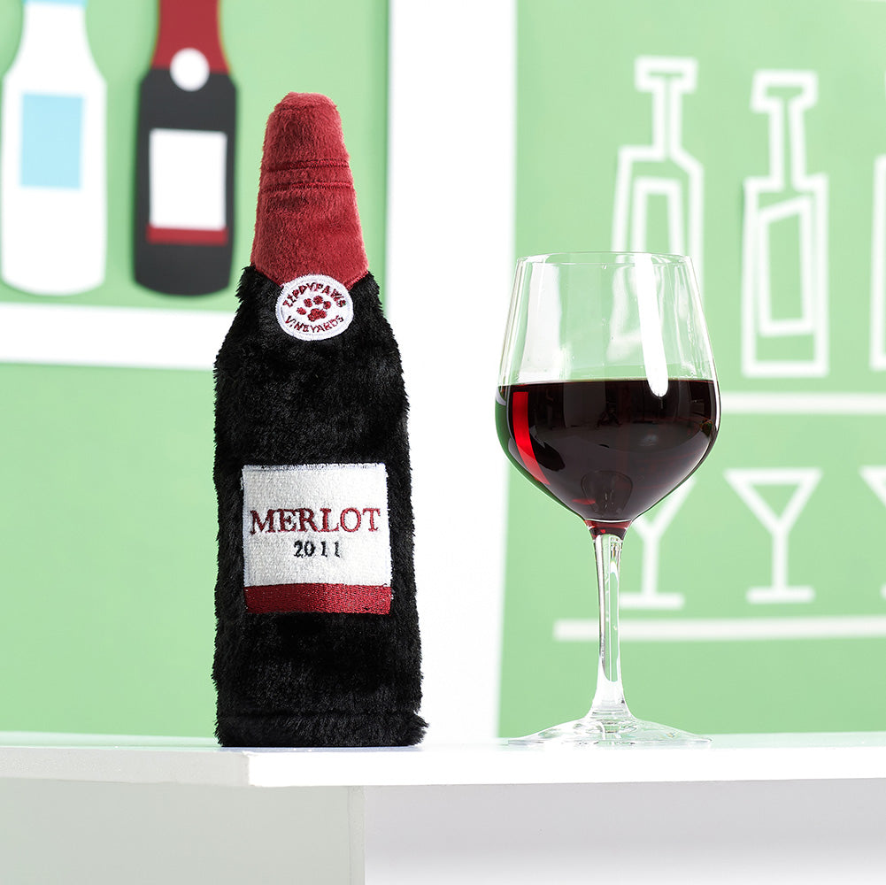 Peluche bouteille de vin rouge ZippyPaws à côté d'un verre de vin